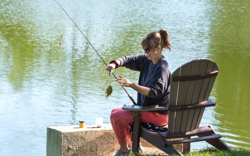 A woman with a fishing rod sits in a chair and holds her small catch