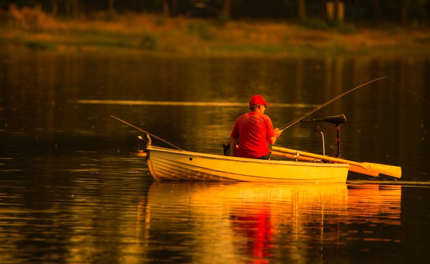 A man fishes from a boat at sunset