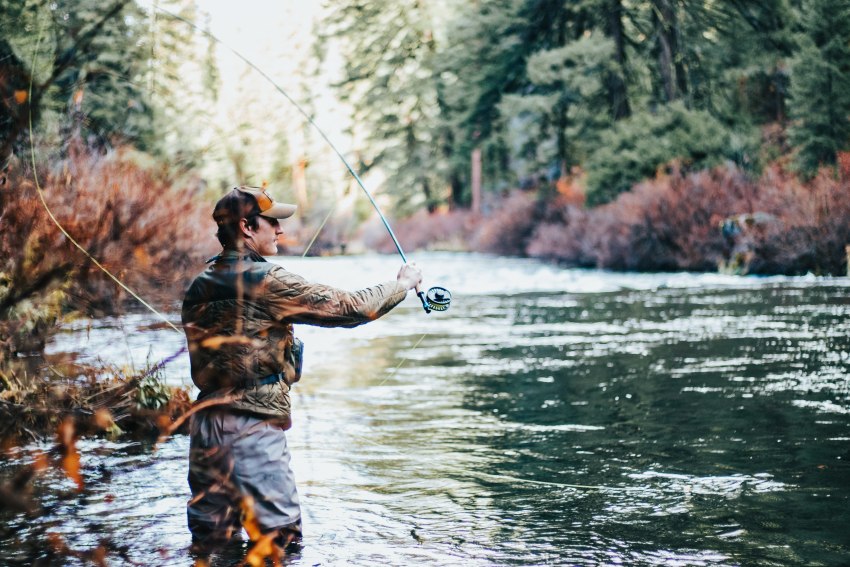 An angler casts a fly rod in a picturesque river in the fall