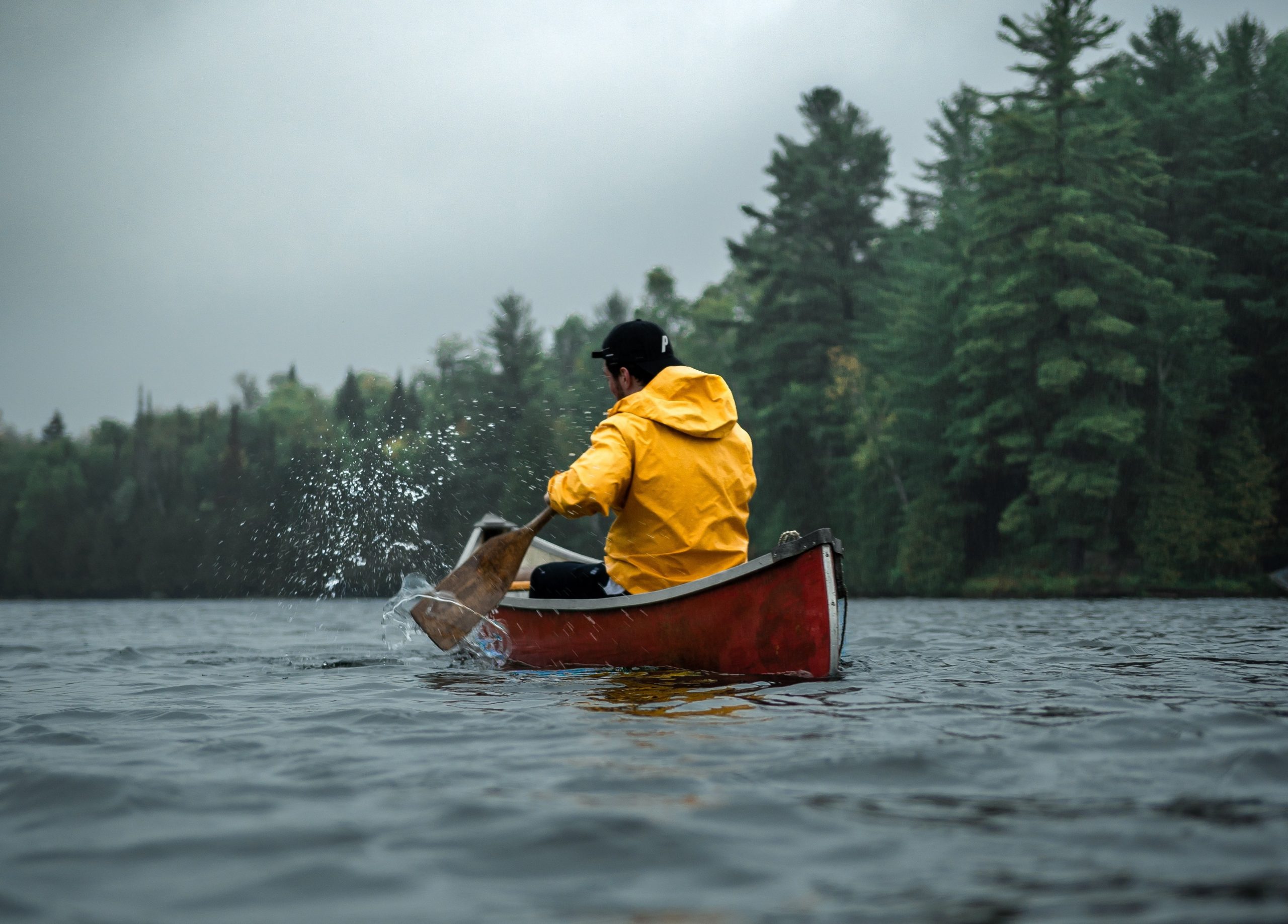 A man wearing a yellow coat paddles his red canoe on the water