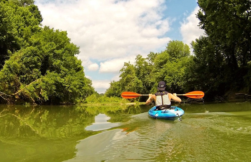 A man with an orange paddle is kayaking on Drakes Creek river