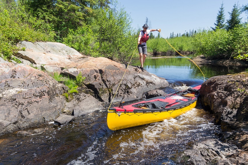 A yellow Nova Craft Prospector 16 canoe, loaded up with gear, is guided between rocks by a male paddler 