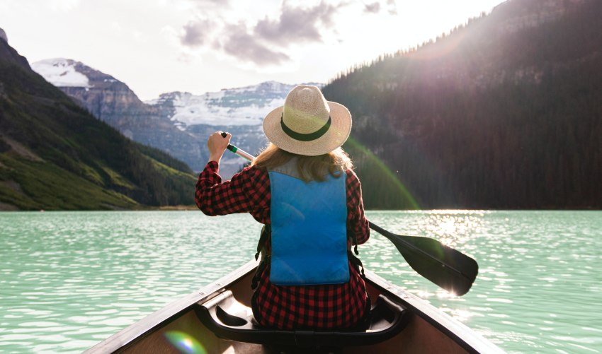 A lady paddles her canoe on a picturesque mountain lake