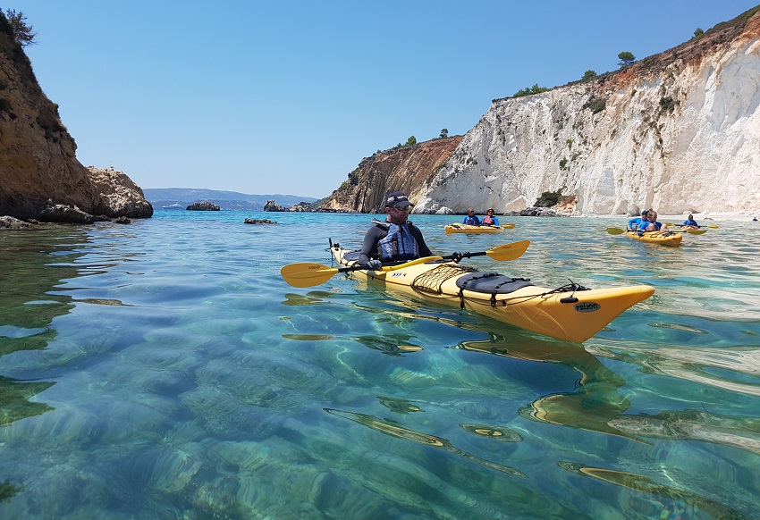 A group of paddlers in yellow expedition kayaks crosses a picturesque bay