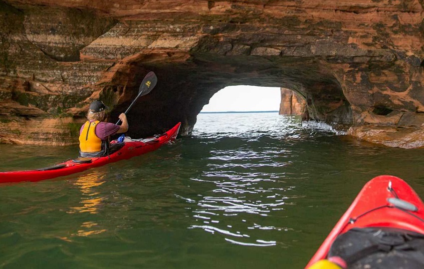 Two red kayaks with paddlers sail in a sea cave