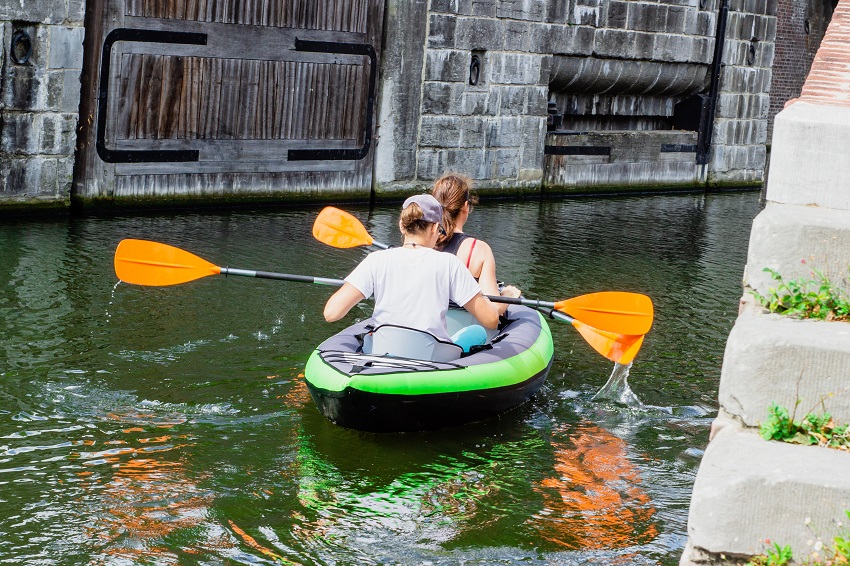 Two women paddle a green inflatable kayak on a water channel