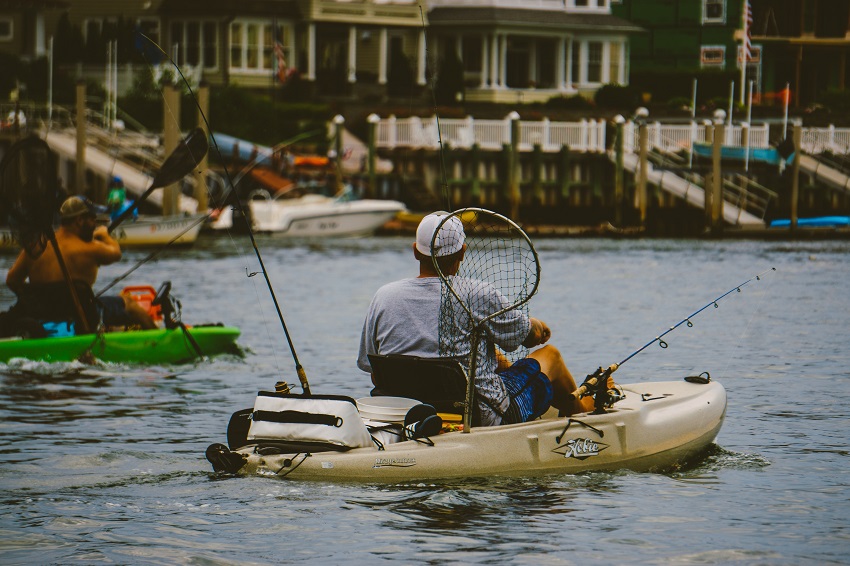 An angler pedals a white kayak, carrying various fishing gear