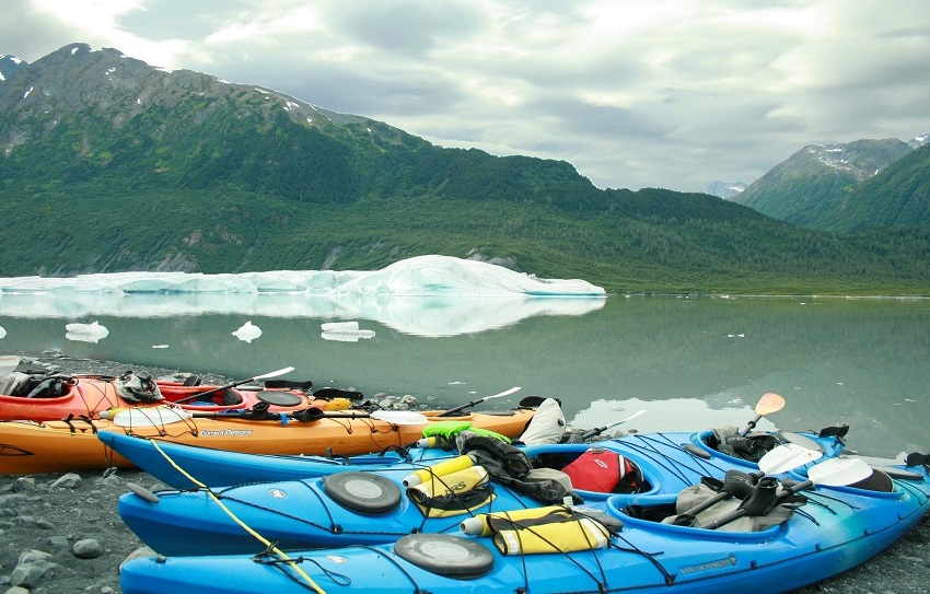 Several kayaks of different colors are parked on a lake shore