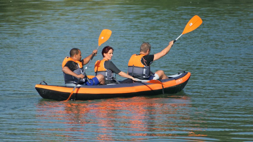 Two men and a woman in orange lifejackets paddle an inflatable kayak