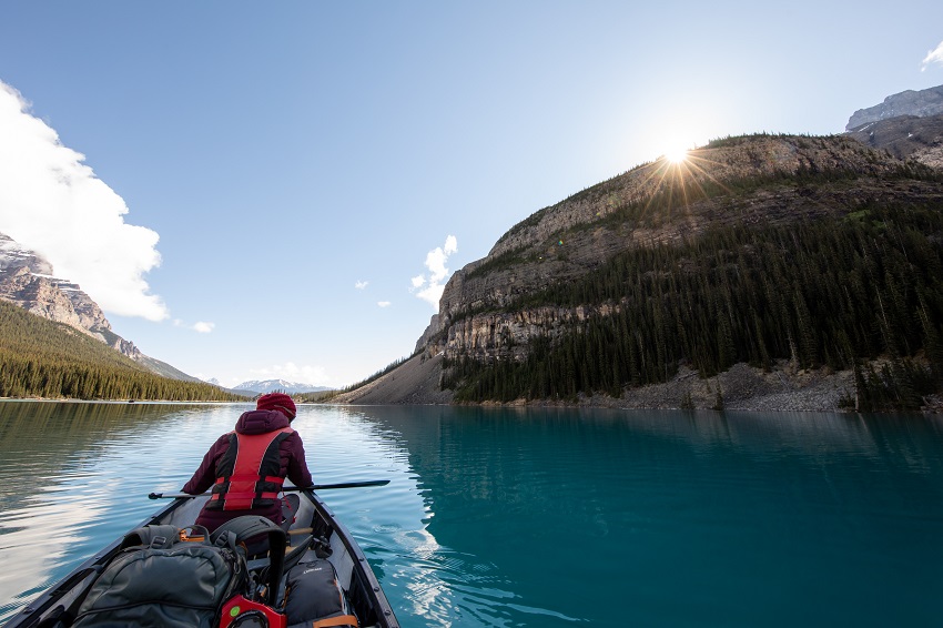 A man in a red PFD paddles his canoe on a beautiful mountain lake 