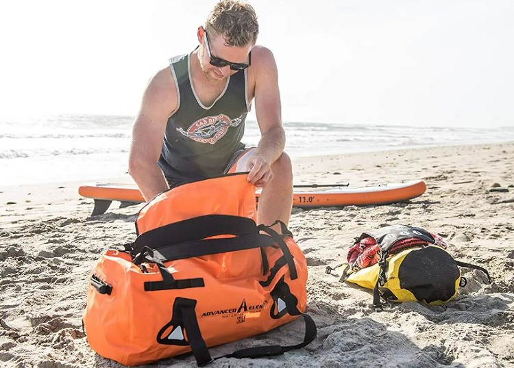 A man packs his waterproof duffel bag on the beach