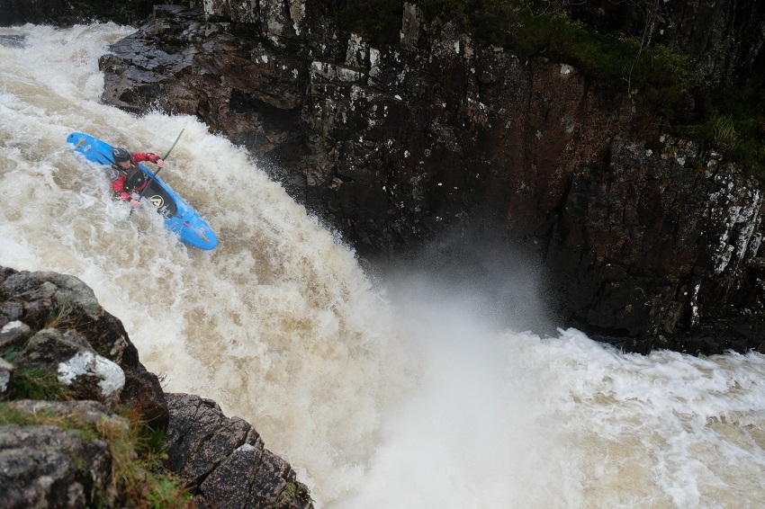 A man paddles a blue kayak in the whitewater