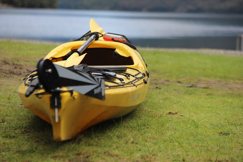 A yellow kayak with a paddle is on a green grass near a river.