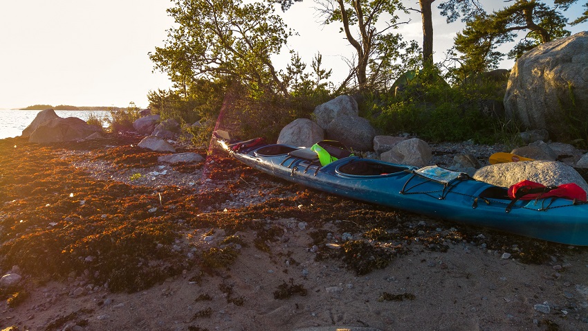 A blue kayak with PFDS is on beach. 