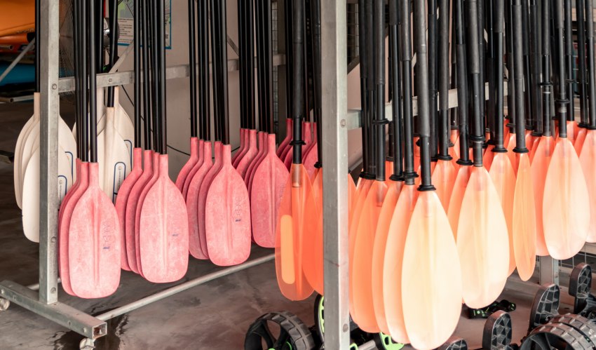 Multiple orange and red paddles hang on a rack