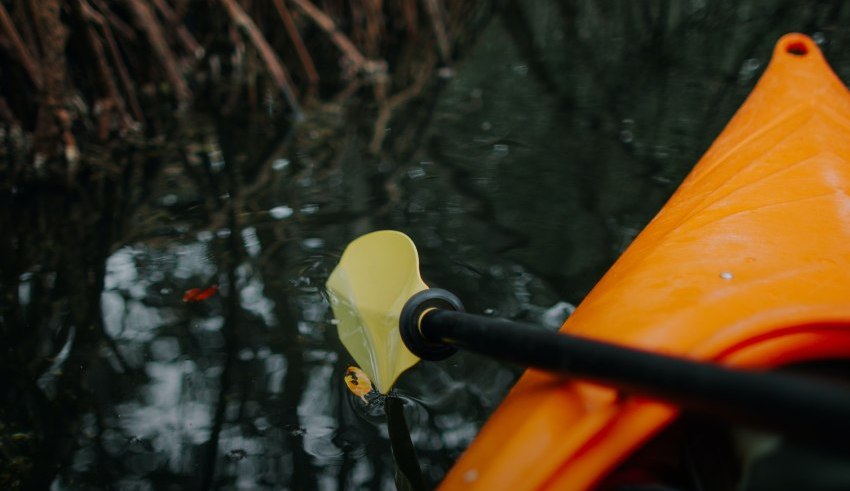 A yellow paddle touches water from an orange kayak's bow