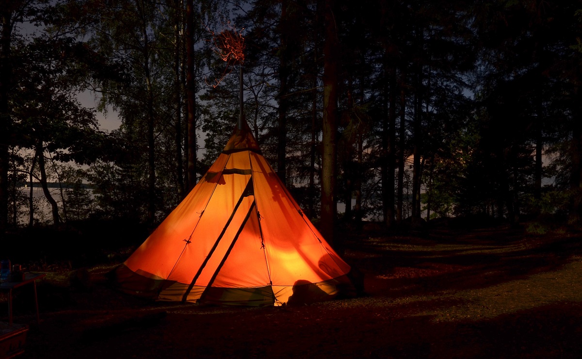 A tent with a stove jack pitched in the woods at night