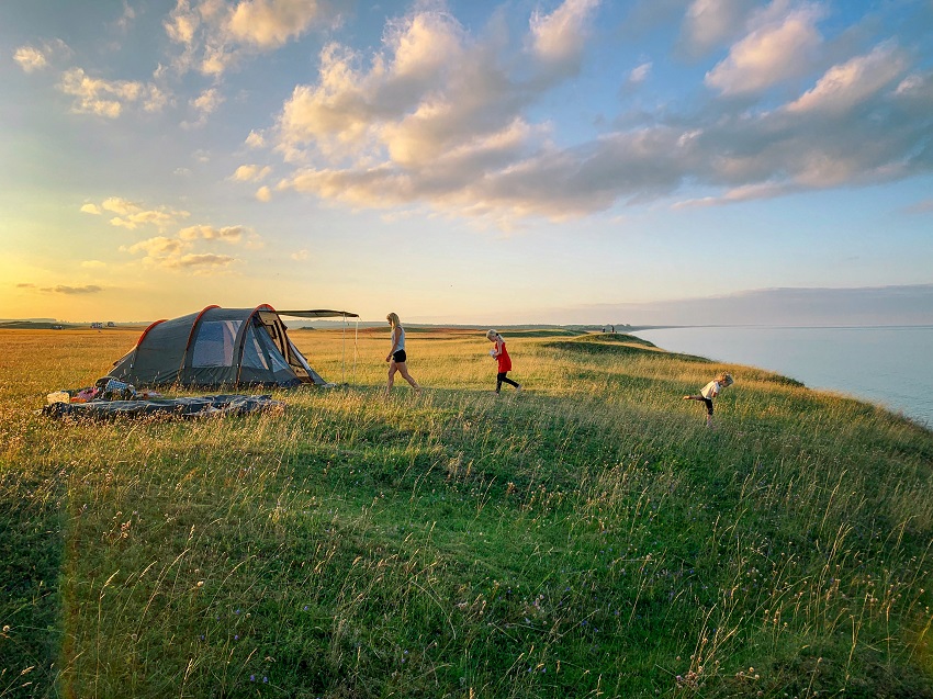 A family plays near a tunnel tent at sunset