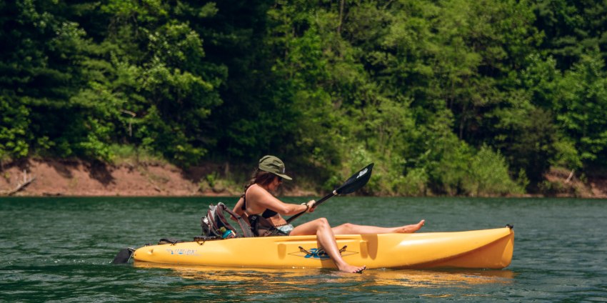 A lady paddles her yellow kayak on a sunny day 