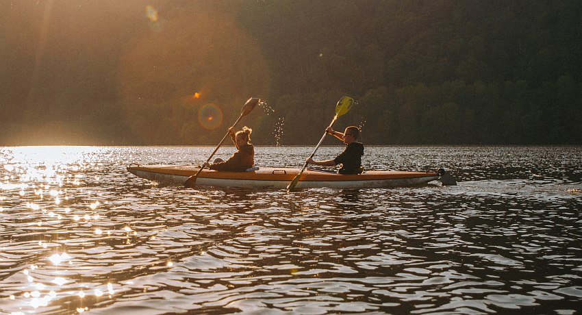 A couple paddles their tandem plastic kayak in the sunlight