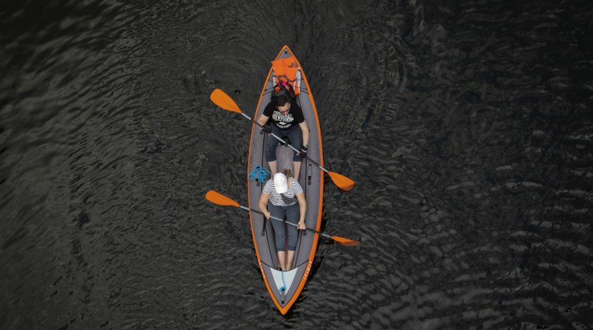 A couple paddles an inflatable grey-orange kayak