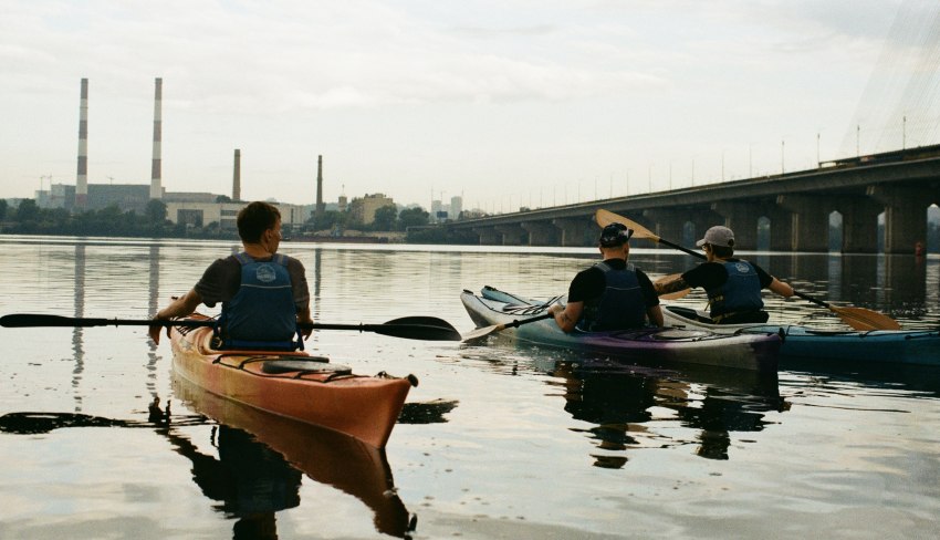 Three men paddle their kayaks in urban waters