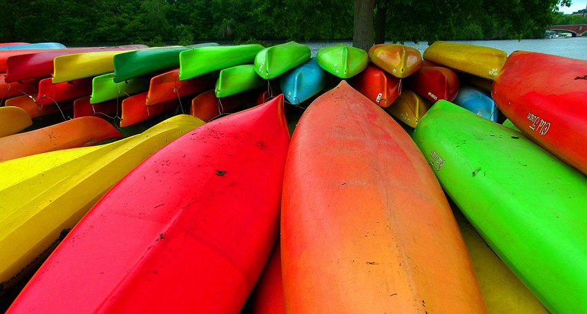 Multiple kayaks of different colors are stacked bottom up