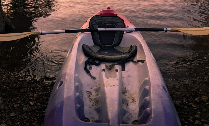 A sit-on top kayak with a paddle is parked on shore 
