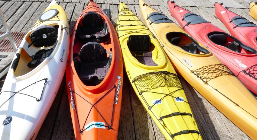 Several kayaks of different colors lie on a pier