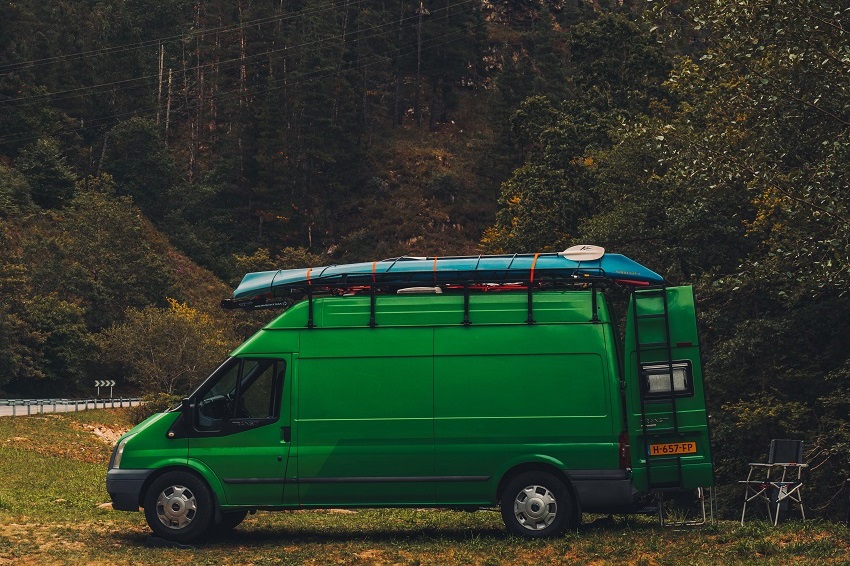 A green van with a blue kayak and white/black paddles on its roof stands on the roadside