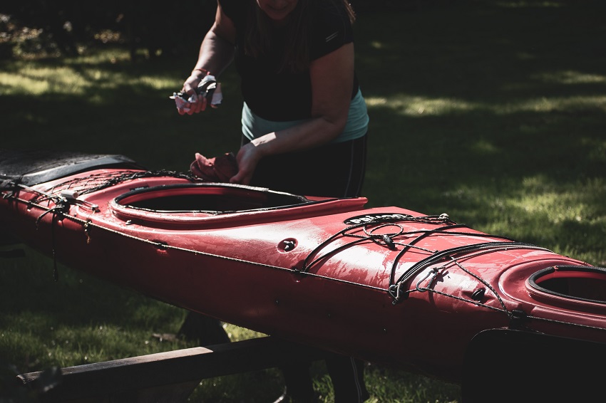 A woman cleans her red kayak outdoors
