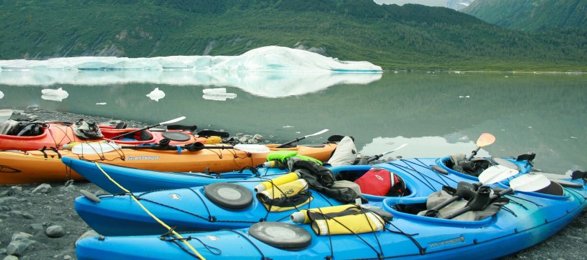 Multiple kayaks of different colors with the camping gear and paddles inside them