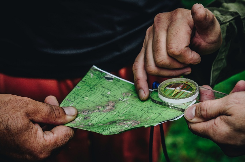 Three human hands hold a map and a compass