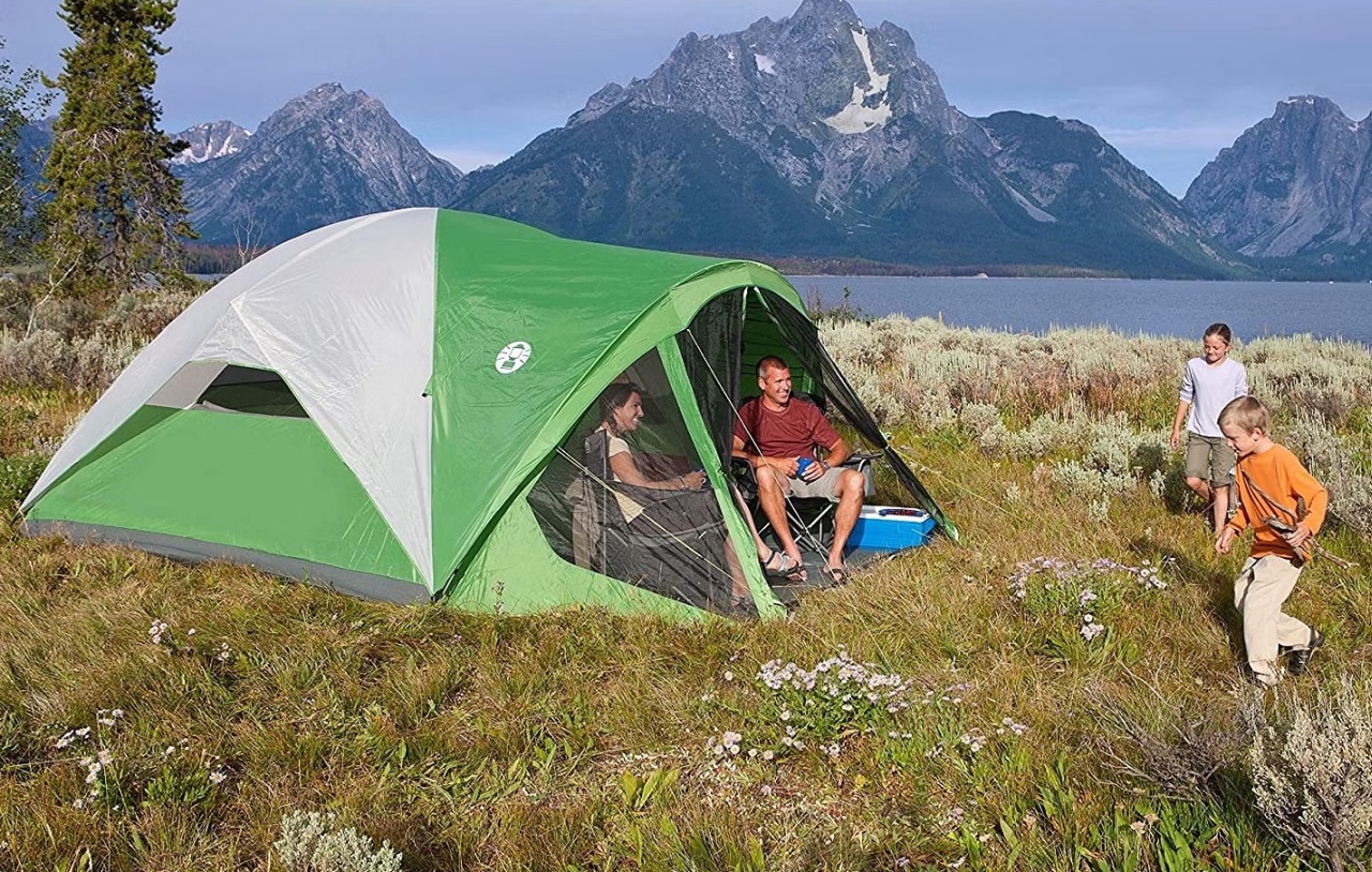 A family sits in a white and green camping tent, pitched outdoors