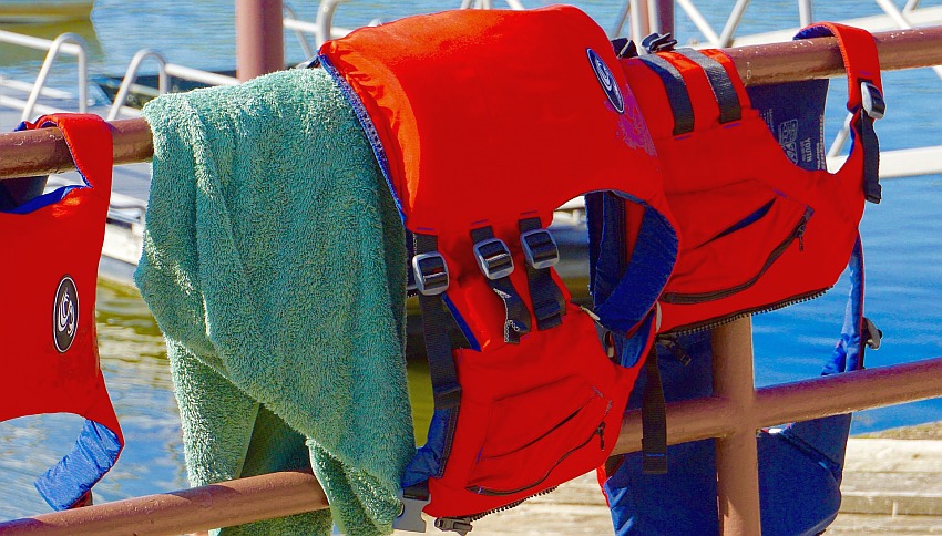 A red life jacket and a green towel hang on a rack