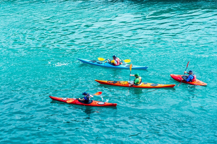 A group of men paddles their kayaks in the open waters