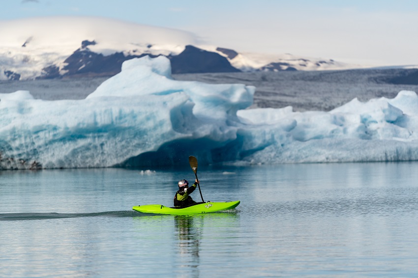 A man paddles a green kayak in arctic waters