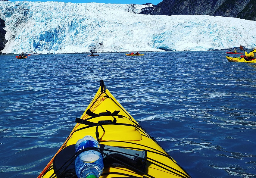 A group of kayakers paddle their boats towards a glacier