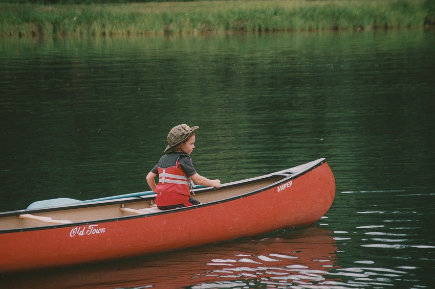 A boy sits in the red Old Town Camper canoe on water