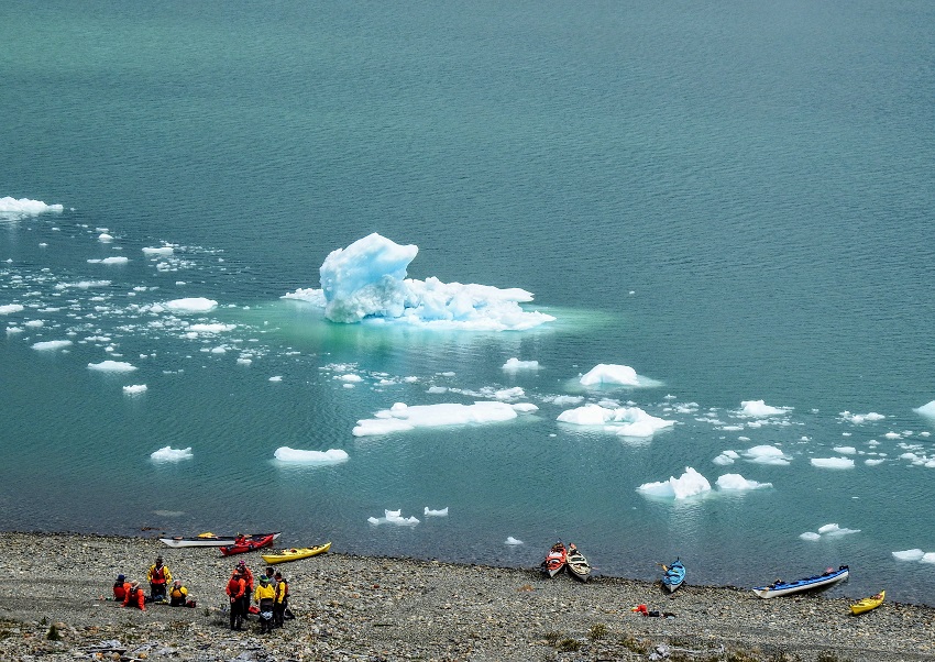 A group of kayakers with their kayaks stay ashore of the lake, covered with blocks of ice and snow