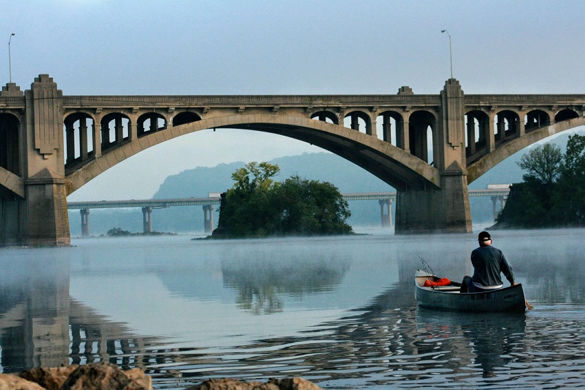 A man paddles his aluminium canoe towards the bridge