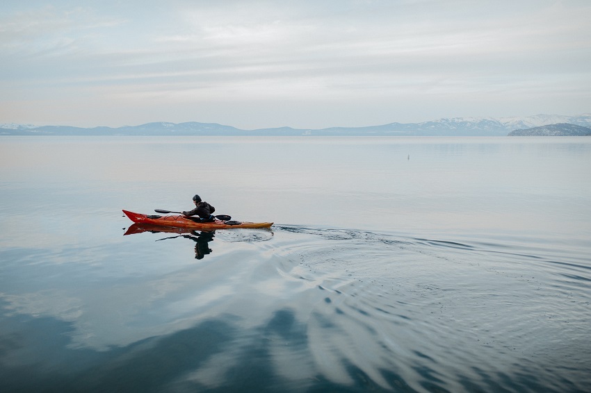A man paddles his orange kayak on the open water