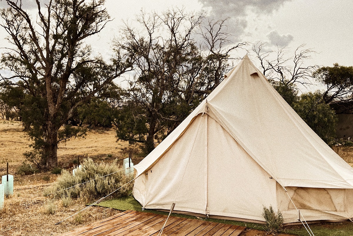A canvas tent with closed doors and wooden flooring is pitched among trees