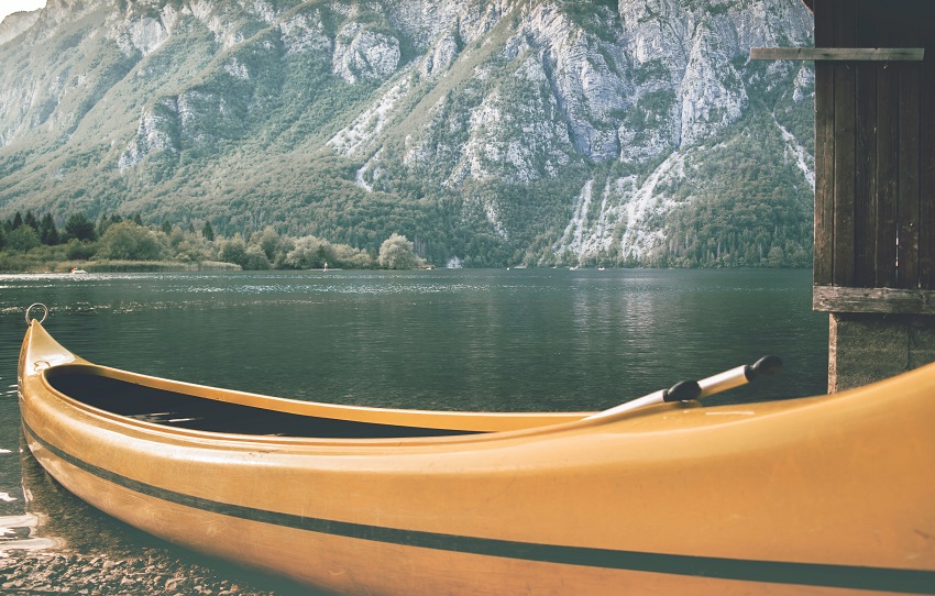 A yellow canoe with paddles inside lies on a lake shore