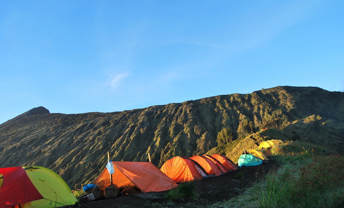Several tents of different colors are pitched in the mountains