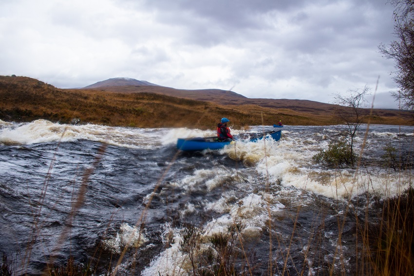 A man in a blue canoe runs the whitewater rapids