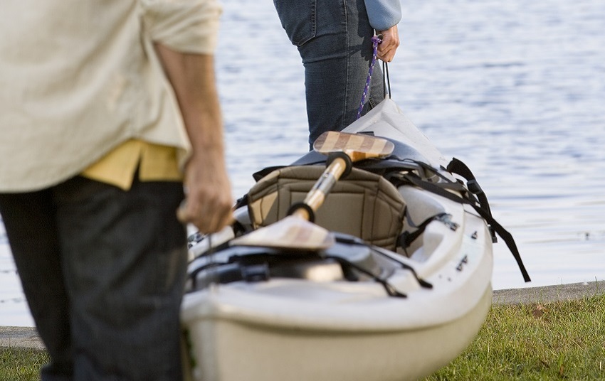 Two people carry a plastic kayak with a paddle on it