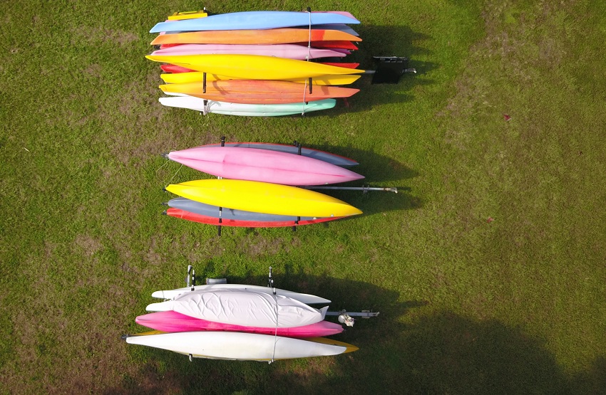 Three trailers with multiple kayaks of different colors are parked in the field