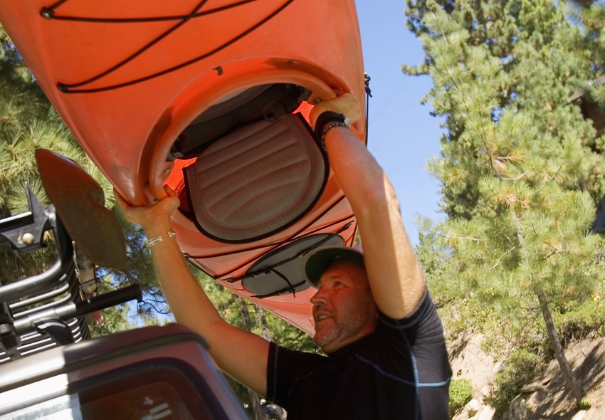 A man loads a red plastic kayak onto his vehicle