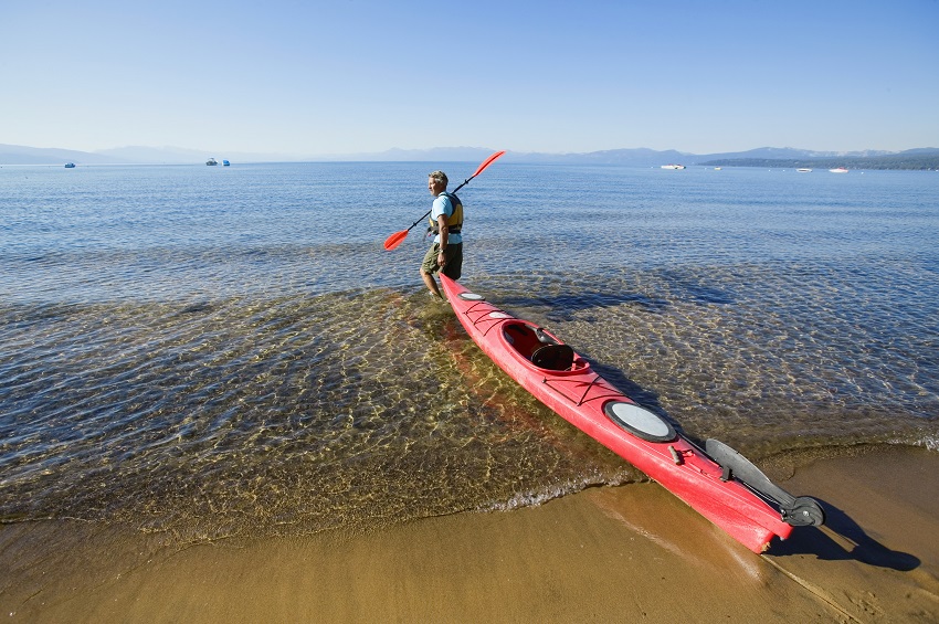 A man drags a red plastic kayak towards the water